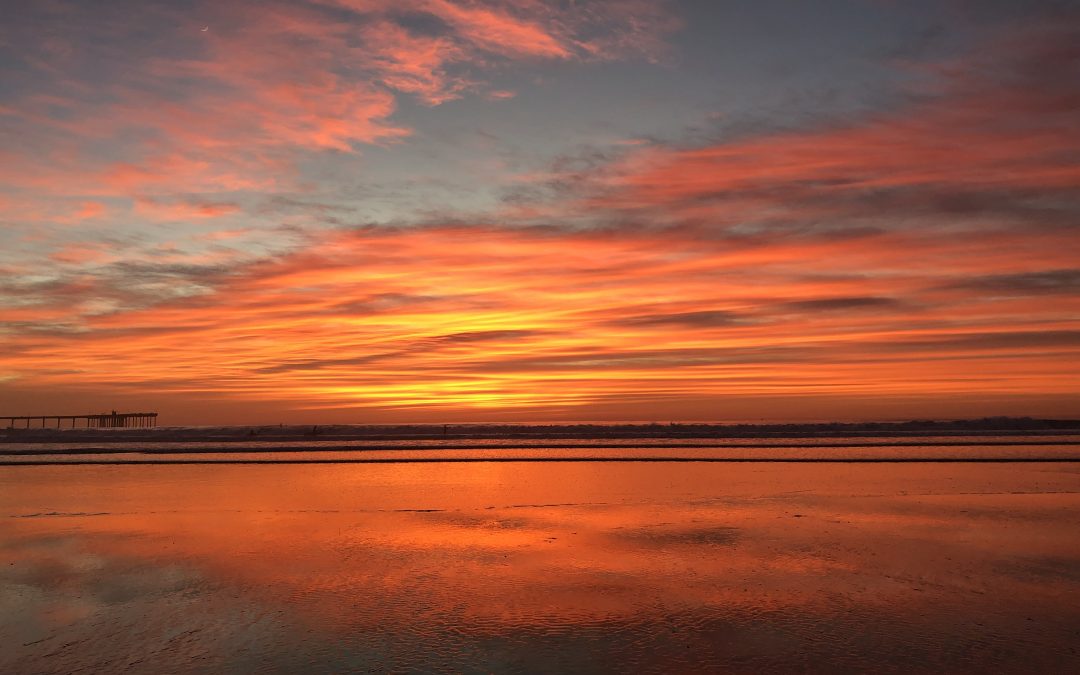 Sunset over a beach with vivid orange and pink clouds reflecting on wet sand.